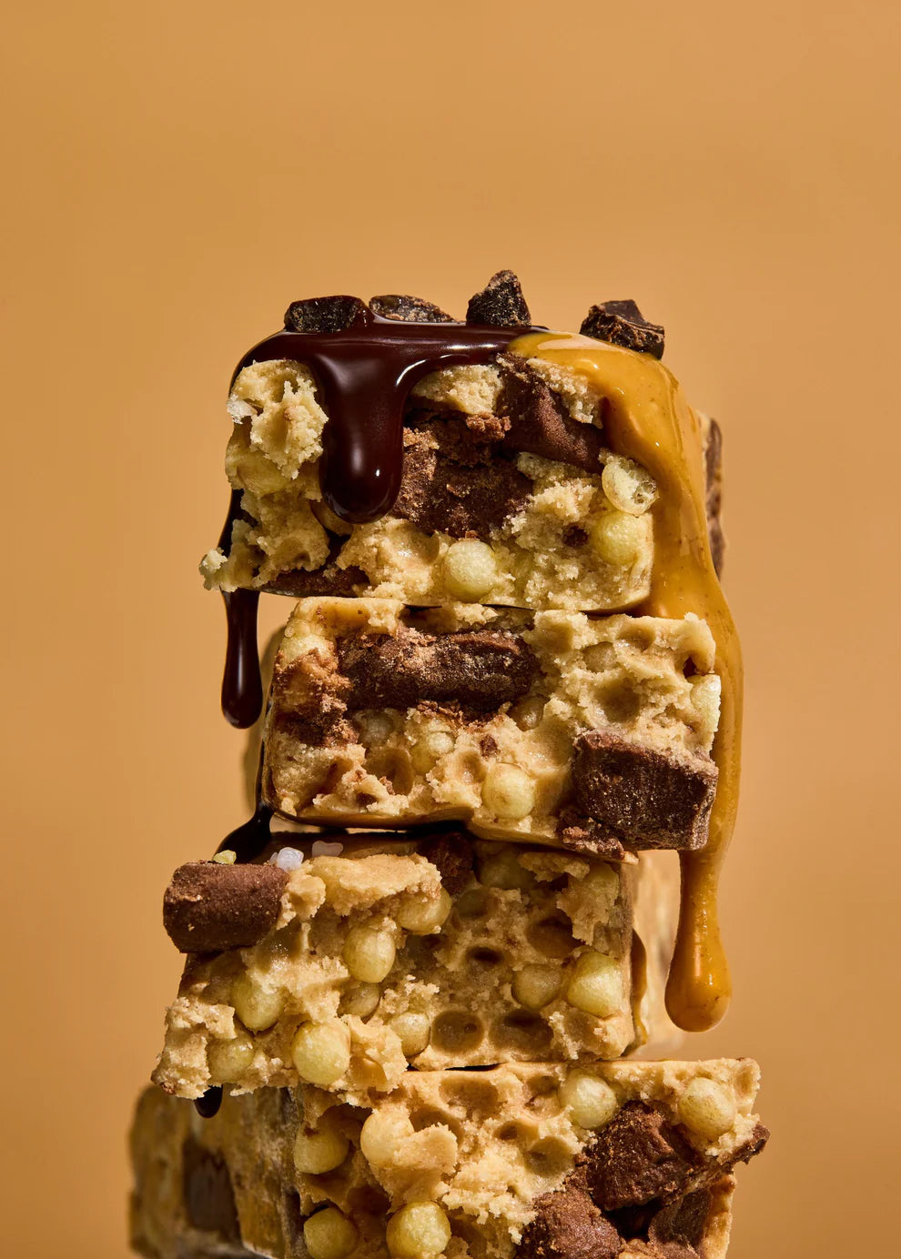 Stack of cookie bars with chocolate and peanut butter drizzle on a brown background