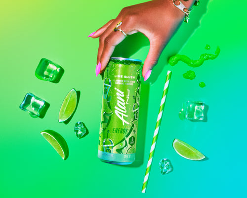 Hand holding a Alani Nu Lime Slush energy drink can with lime slices and ice cubes on a bright green background